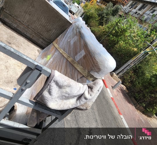 רהיטים עטופים בניילון על עגלת הובלה ברחוב עירוני